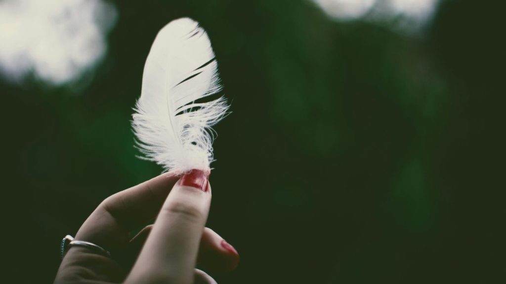 Mano femminile che tiene una piuma tra le dita, simbolo di leggerezza, libertà interiore e guarigione spirituale.